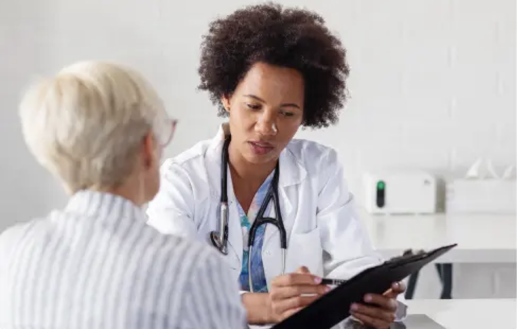 Female doctor holding clipboard talking to elderly female patient