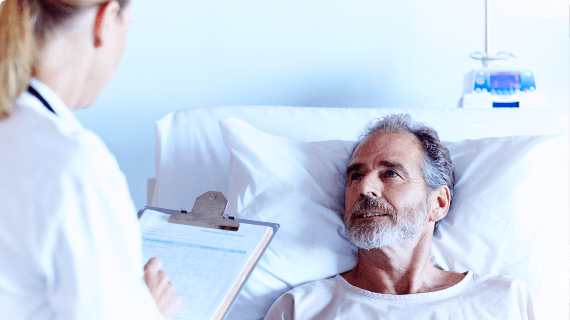 Doctor with clipboard talking to patient in hospital bed