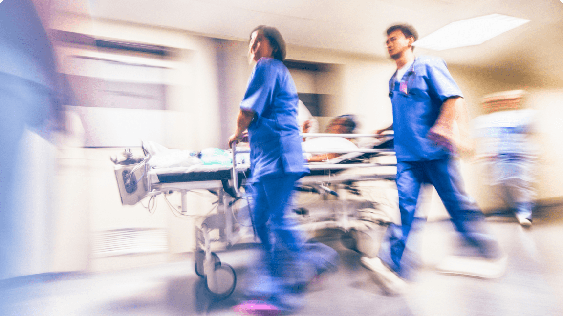 Two doctors in blue scrubs wheeling patient on hospital bed