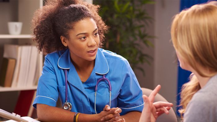 Close-up of female doctor in blue coat consulting with a female patient in a doctor's office.