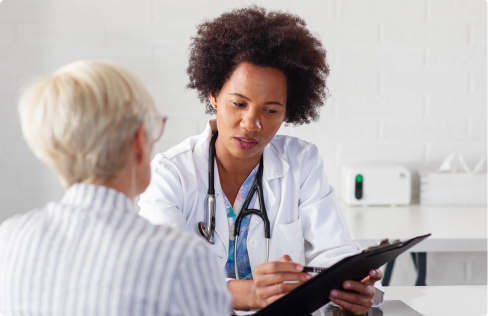 Female doctor holding clipboard talking to elderly female patient